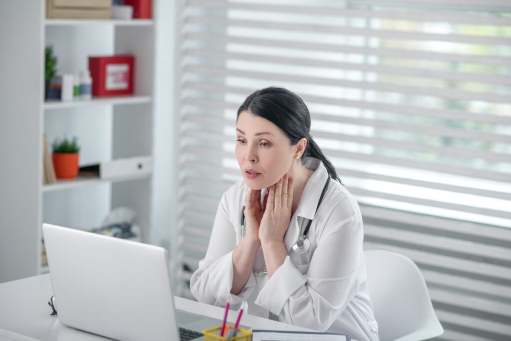 Woman telemedicine physician telehospitalist in white coat in front of laptop.